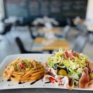 Salade de prosciutto et melon tranché frais avec réduction balsamique, servie dans un restaurant lumineux.