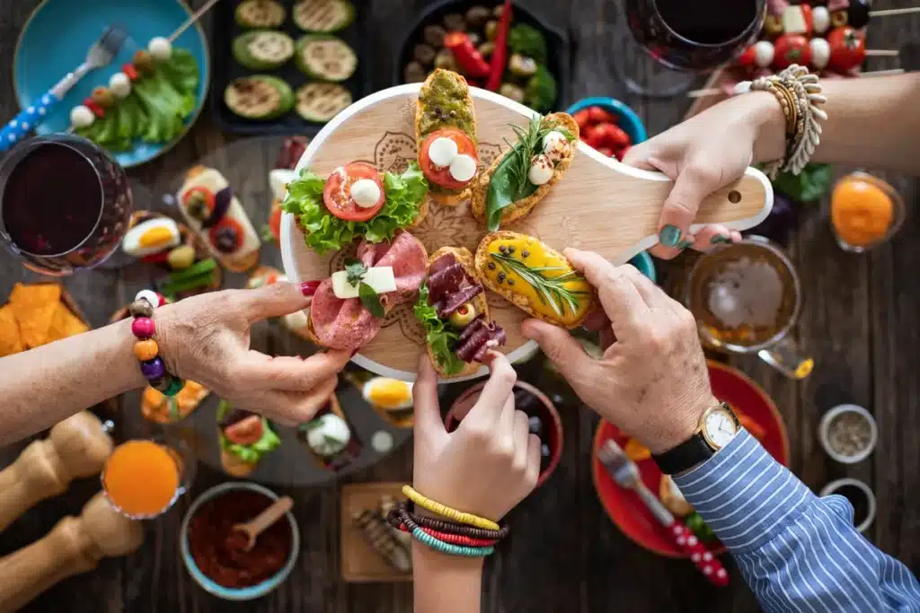 Mains partageant des amuse-bouches colorés sur un plateau en bois lors d'un repas convivial entre amis.