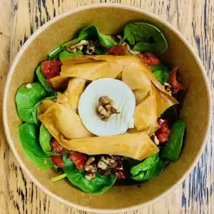 Salade d'épinards frais, chèvre chaud croustillant, noix et tomates séchées dans un bol.